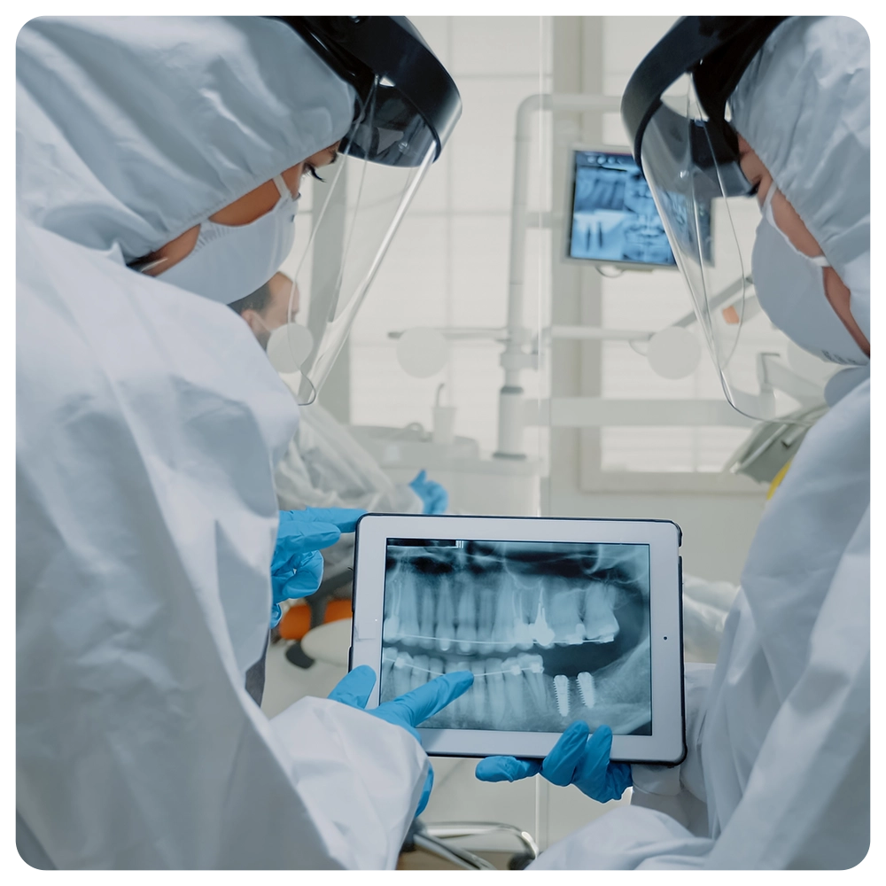Professional dentists using technology for oral examination while wearing protection suits at dental clinic