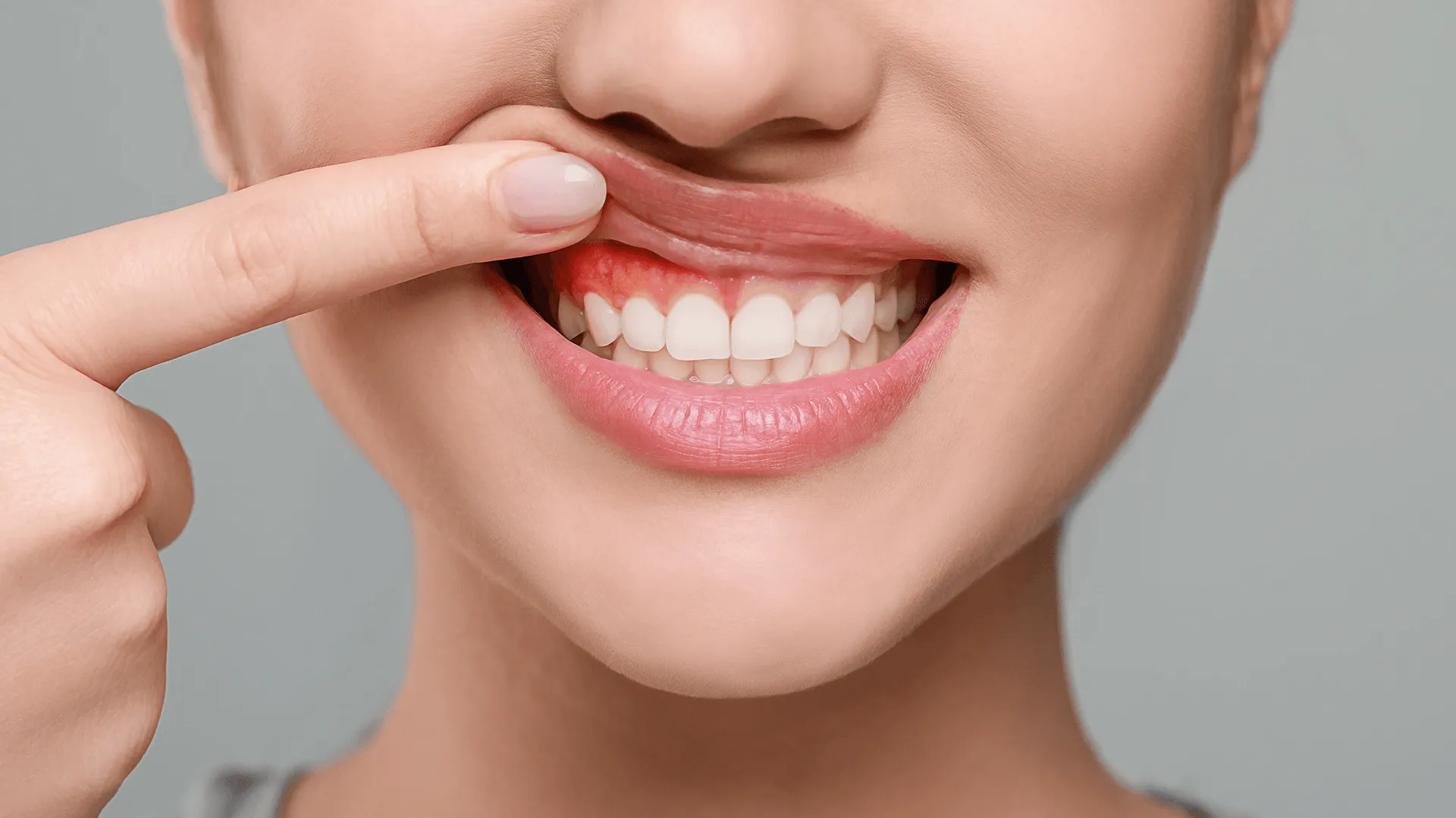 Woman showing inflamed gum on grey background, closeup