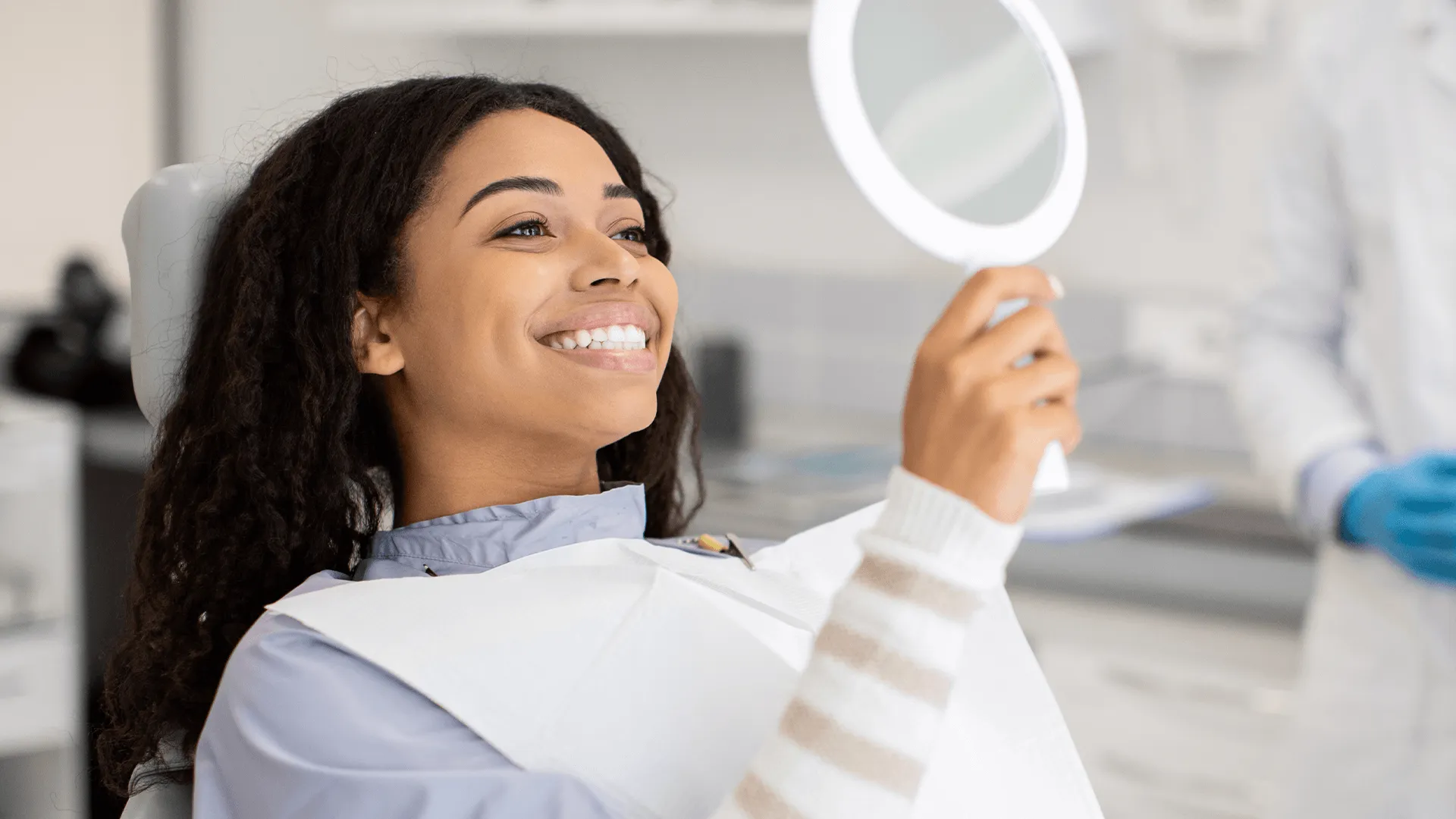Happy Black Female Patient Looking At Mirror After Dental Treatment In Clinic