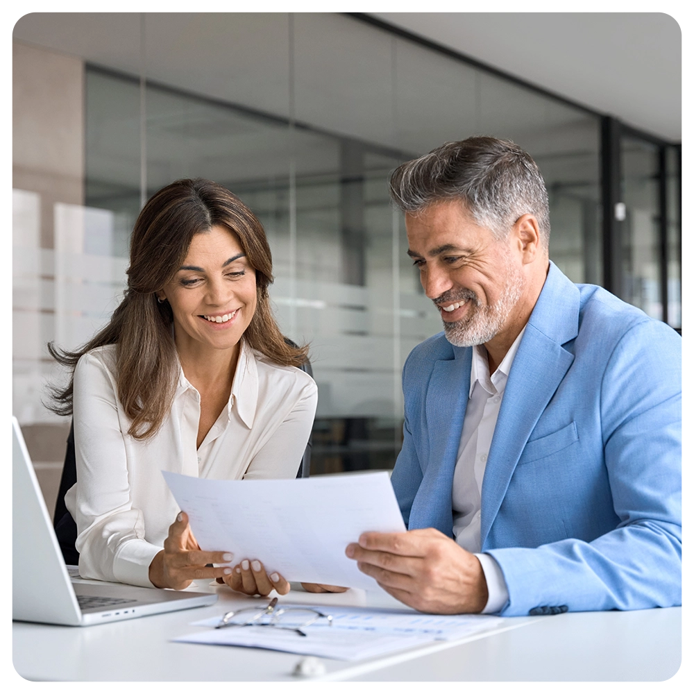 Two happy busy middle aged professionals man and woman business leaders partners checking document reading financial report talking working together on laptop computer in office at corporate meeting.
