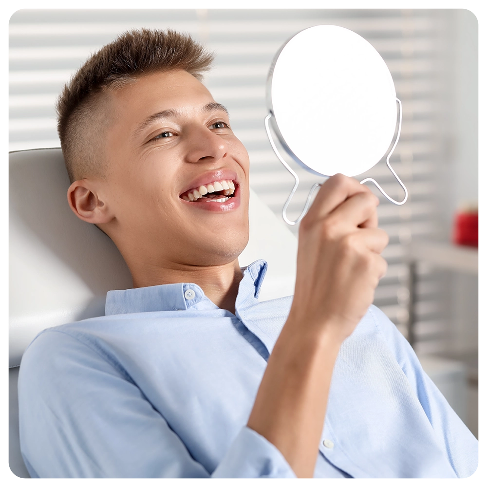 Happy young man with mirror in clinic, closeup.