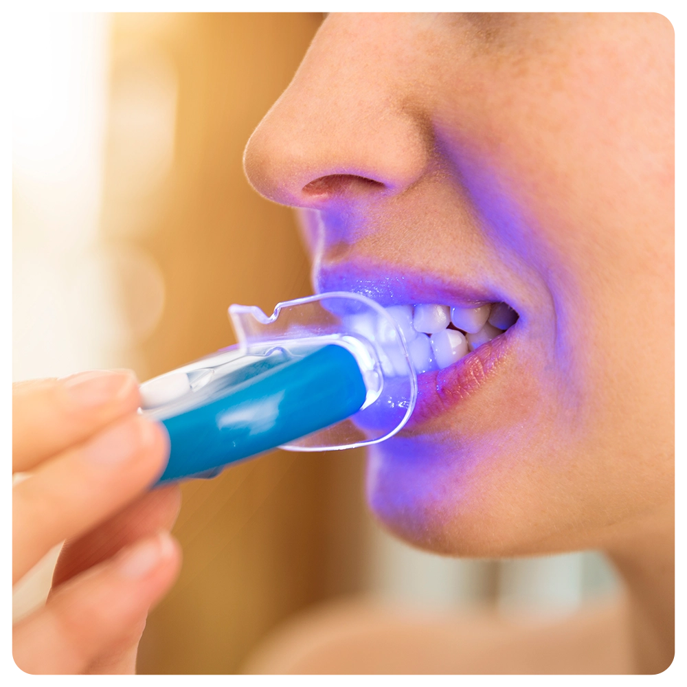 Woman is whitening teeth with special toothpaste and LED light at home. Beauty concept