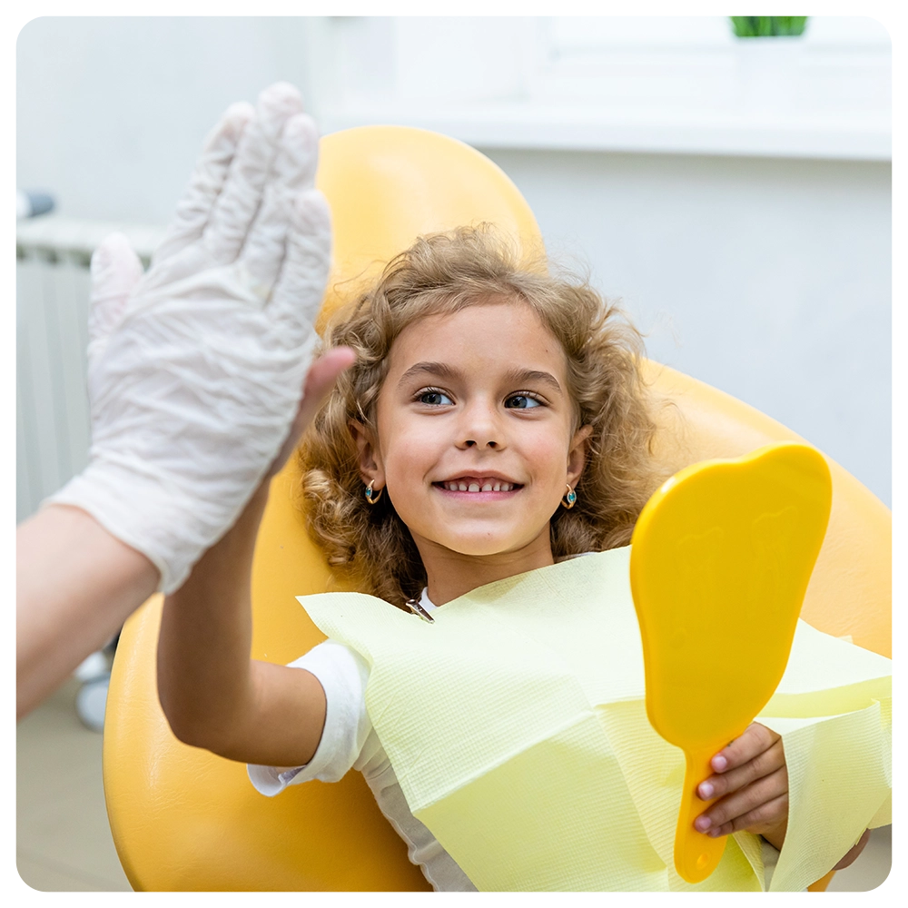 Little patient girl sitting in a chair gives a high five to a pediatric dentist after dental treatment at a clinic with modern equipment