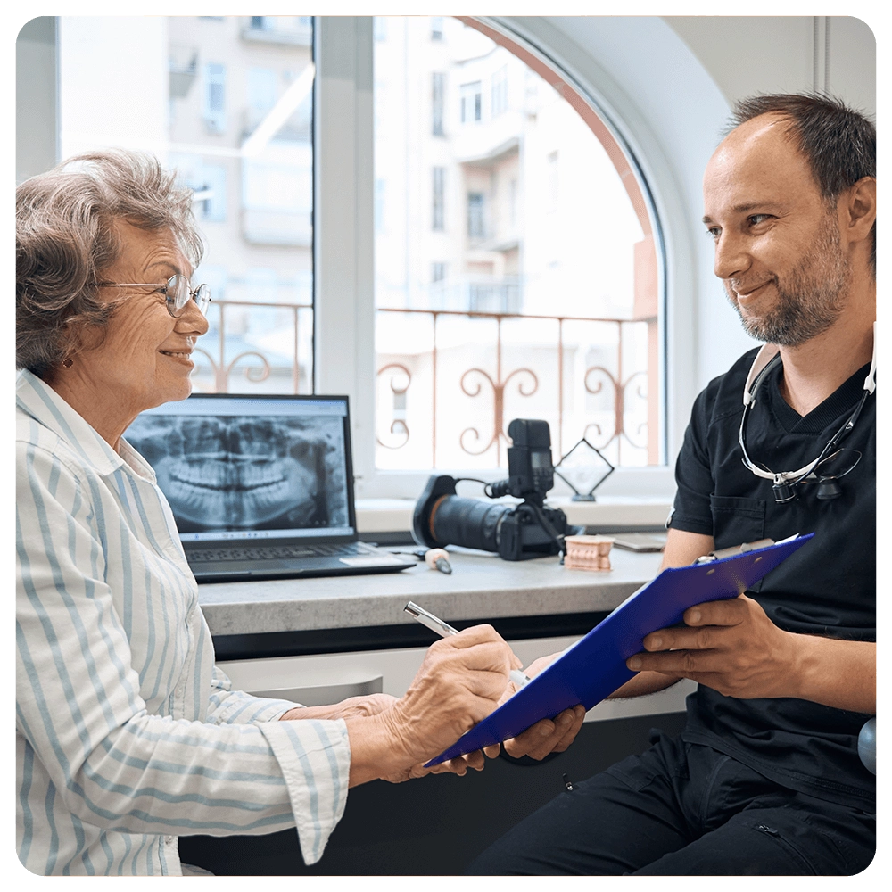 Senior woman signing dental paperwork with her dentist.