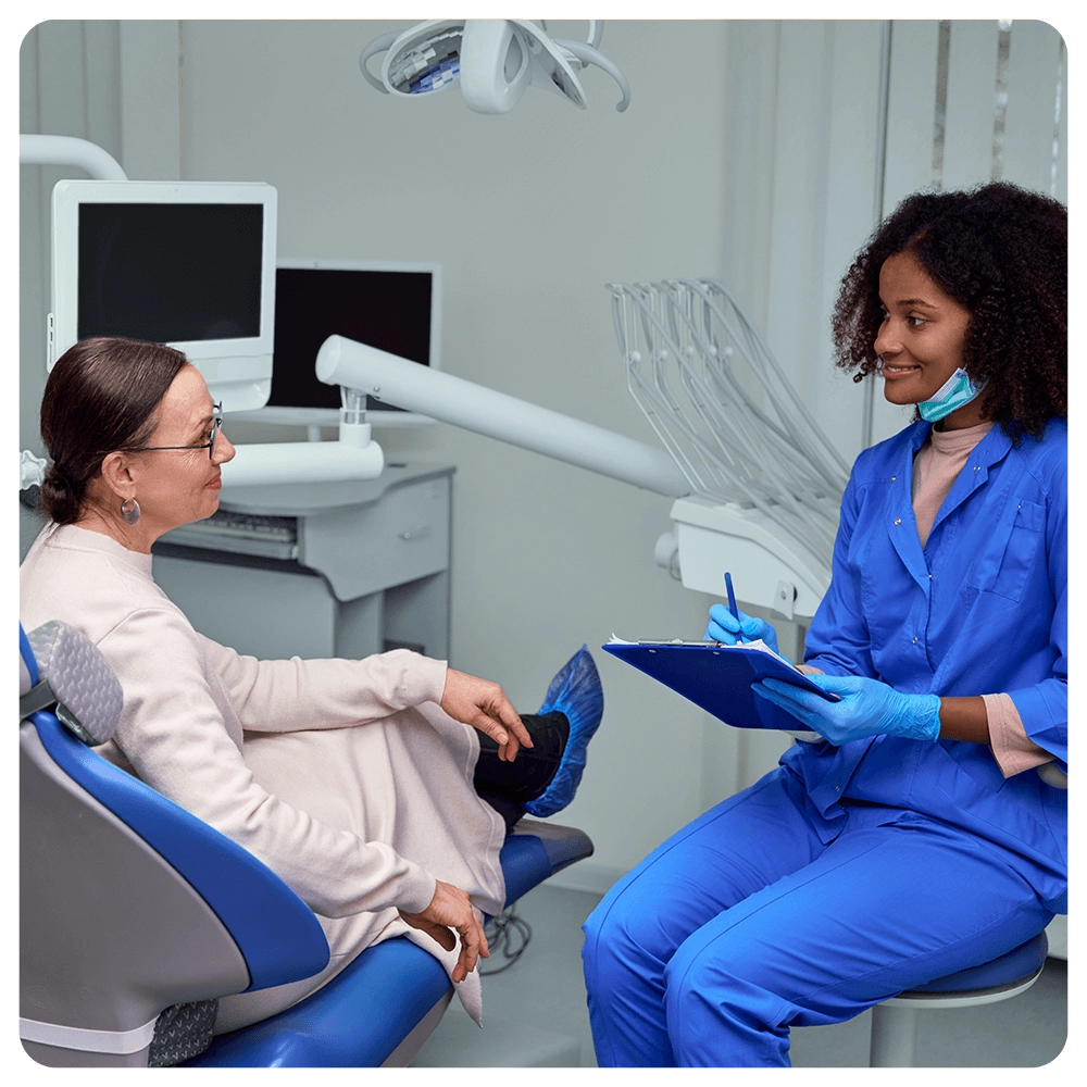 Dentist consulting senior patient, taking notes on clipboard