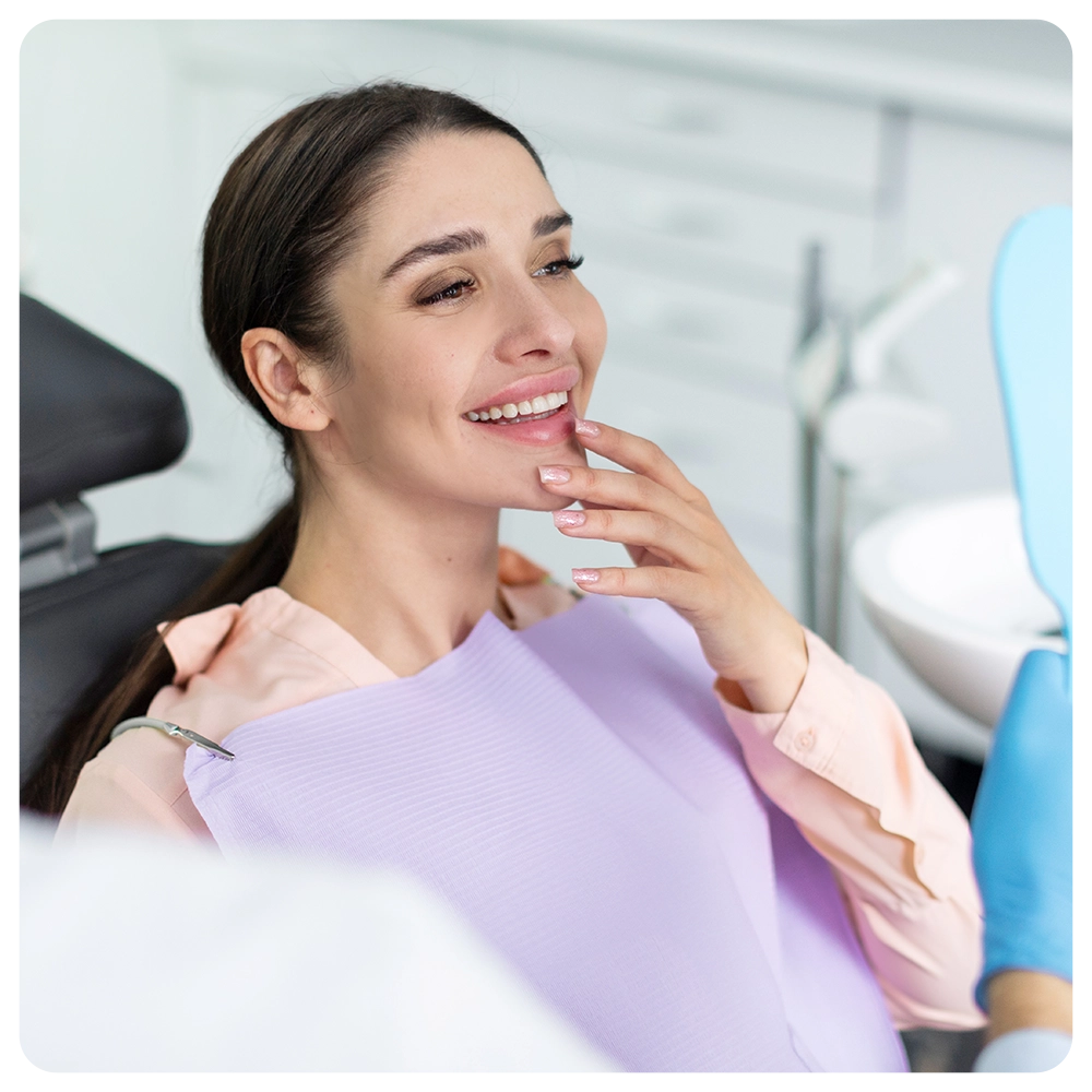 Smiling woman looking in mirror after dental procedure in clinic, enjoying result of teeth whitening result