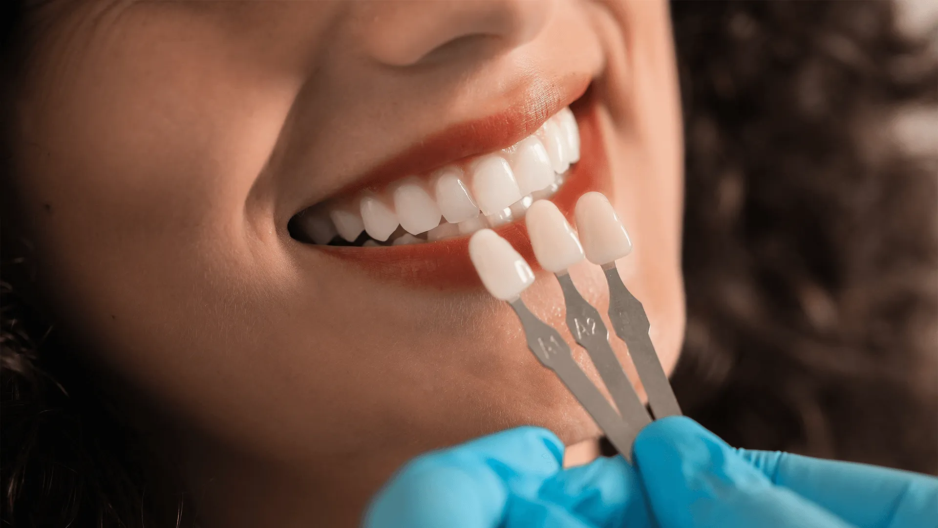 Patient looking in mirror while doctor holding teeth color chart in clinic, closeup. 
